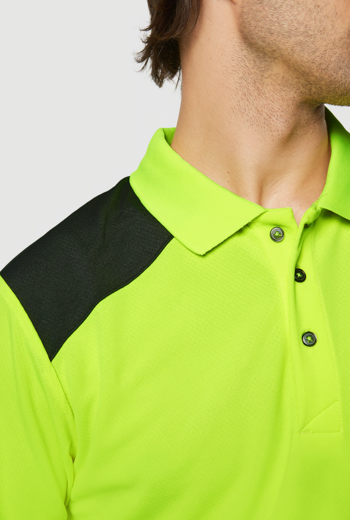 A person is shown from the side wearing a CAT Hi Vis Performance Polo in neon green with moisture-control fabric, black shoulder accents, and short sleeves. The CAT logo is on the buttoned collar, set against a plain light gray background.
