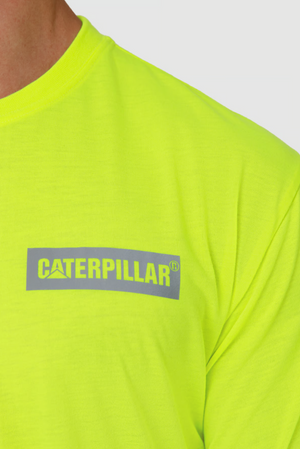 Close-up of a person in a vivid yellow-green CAT Triton Block Tee, crafted from 100% cotton with the gray "Caterpillar" logo on the chest. The fabric is designed for moisture-wicking and is set against a plain white background.