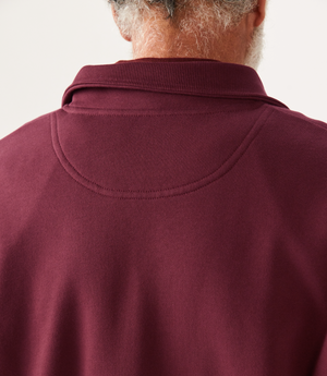 Close-up of the back of a person in a maroon RM Williams Mulyungarie Fleece, showcasing stitching on the brushed cotton fleece fabric and their short, curly gray hair. The background is plain and light-colored.