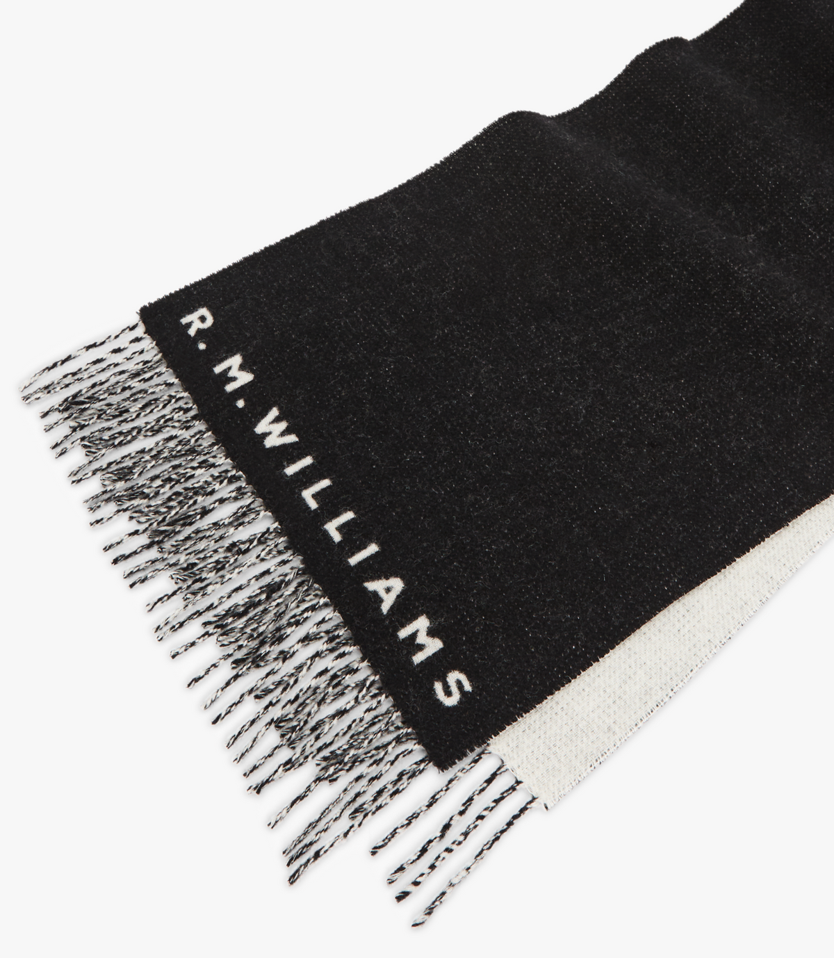 The RM Williams Logo Scarf features a black wool design with tassel trim and mixed black and white fringe, adorned with the "R.M. Williams" logo woven in white near the end for an elegant touch.