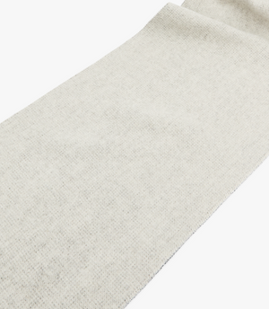 The RM Williams Logo Scarf is made of soft, cream-colored wool with a textured surface and subtle woven pattern. It's elegantly folded on one side and finished with a delicate tassel trim along the edges.