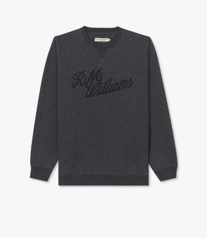 The RM Williams Script Crew Neck is a dark grey cotton blend jumper with ribbed cuffs and hem, featuring "R.M. Williams" embroidered in black cursive on the front.