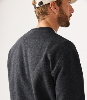 A man in an RM Williams Script Crew Neck and a beige baseball cap faces away from the camera against a light-colored background.