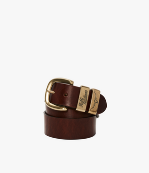 The RM Williams Drover Belt, intricately coiled and crafted from brown vegetable-tanned leather, features an antique brass buckle and a distinctive gold-accented loop engraved with the words "Free Roam." The belt is showcased against a plain white background.