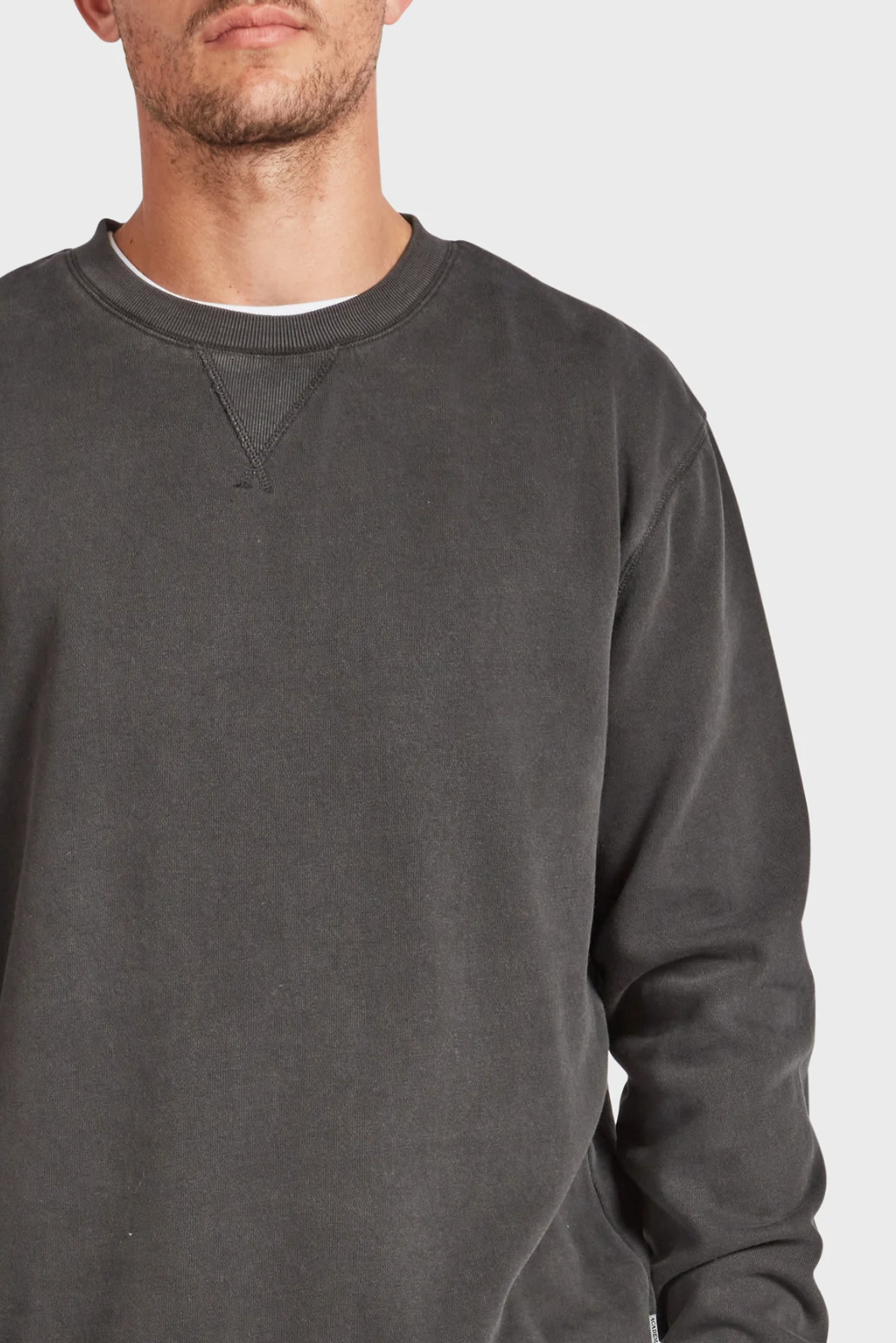 A person wears the Academy Brand Crew Sweat in dark grey over a white undershirt. The photo is cropped to show only the lower face and upper torso against a plain background.