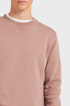 A person wearing the Academy Brand Crew Sweat in light brown over a white t-shirt, shown from shoulders to mid-torso against a plain light background, with their face partially out of frame.