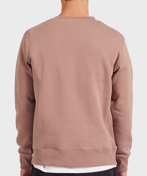 A person is seen from behind wearing the mauve Academy Brand Crew Sweat over a white shirt. The brushed fleece and relaxed fit make it comfortable for everyday wear. The background is plain and light-colored.