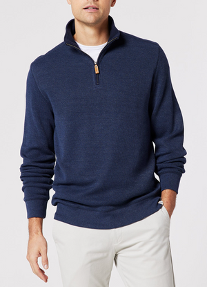 A man wears the Blazer Heather Half Zip Sweat, a navy peached-finish sweater with a half zip, over a white shirt and light pants. He stands against a plain light background with his left hand by his side and right arm slightly bent.