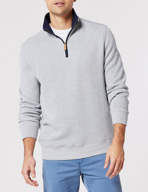 A person wearing the Blazer Heather Half Zip Sweat in light gray over a white shirt and blue pants stands against a plain background. The casual outfit is enhanced by the sweater's dark blue zipper lining, offering a relaxed yet composed look ideal for any casual day.