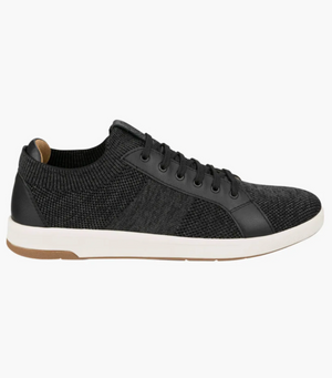 The Florsheim Crossover Knit is a black low-top sneaker with a textured mesh design and knit elements. It features black laces, smooth accents, a cushioned footbed for comfort, and is finished with a white midsole and brown rubber outsole for an elegant, modern look.