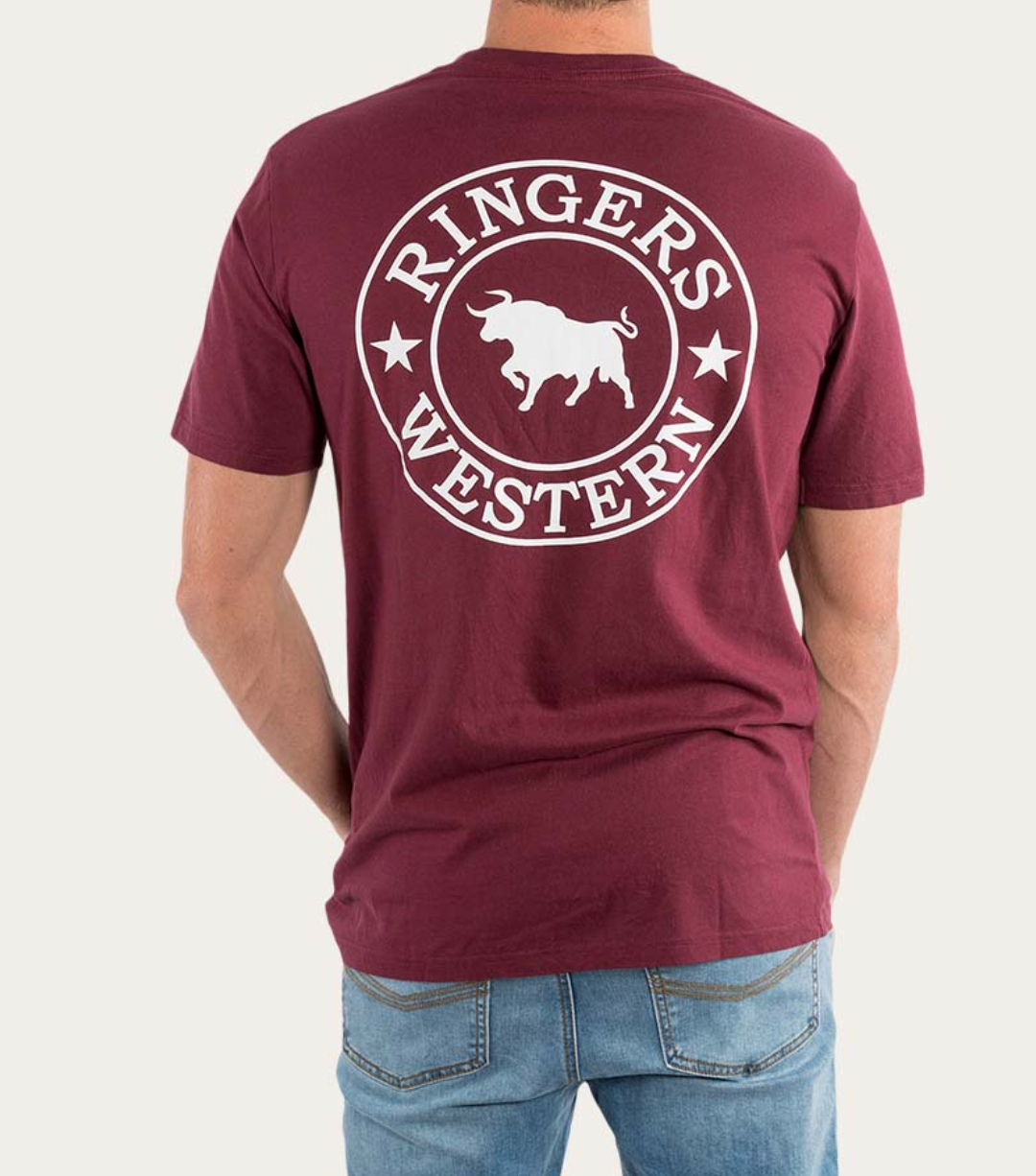 A person is seen from behind wearing a Ringers Western Signature Bull Classic T-Shirt in maroon, featuring short sleeves and a white logo that reads "Ringers Western" with a bull and stars. Made from 100% cotton for comfort and durability, the person pairs this tee with light blue jeans.