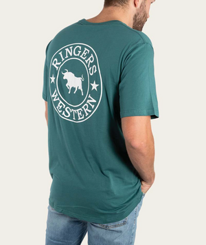 A man in a green Ringers Western Signature Bull Classic T-Shirt, featuring a circular bull and stars logo on the back, made from pre-shrunk cotton, pairs it with blue jeans. He stands with hands in pockets, facing away.