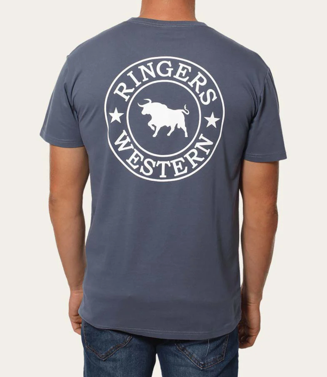 A person sports the Ringers Western Signature Bull Classic T-Shirt in gray, featuring "Ringers Western" and a white bull graphic on the back. Crafted from pre-shrunk cotton, it effortlessly complements their blue jeans, highlighting a laid-back style from behind.