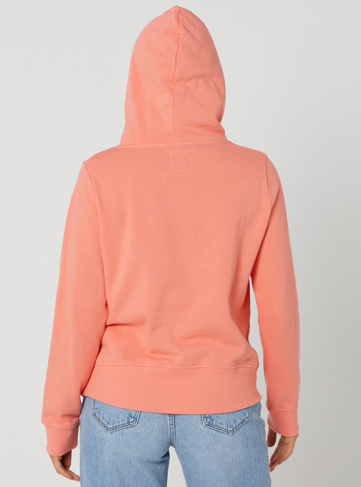 Rear view of a person wearing the Rip Curl Script II Hood in coral, with the hood up, paired with light blue jeans against a plain white background.