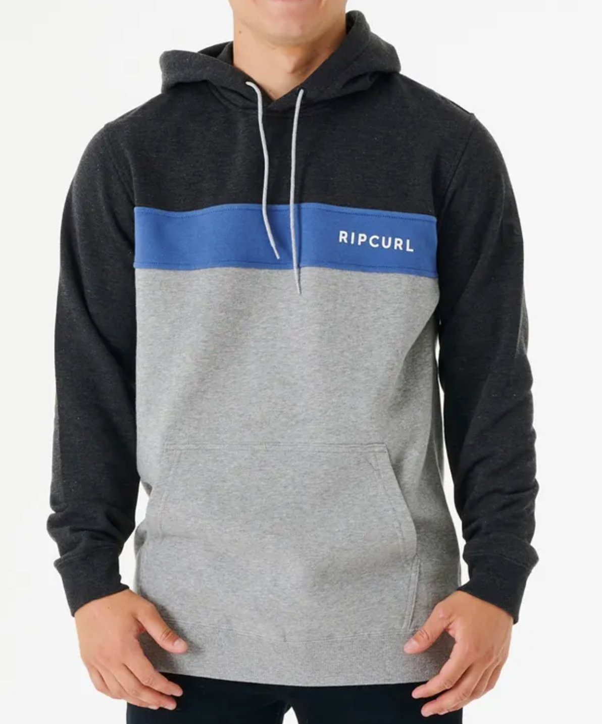A person wears the Rip Curl Undertow Panel Hood, featuring a dark gray upper section, blue stripe with "Ripcurl" text, and light gray lower section. This comfy fleece-lined hoodie has white drawstrings and a front pocket. They stand against a plain white background.