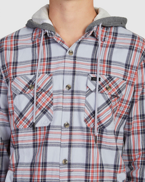 A close-up shows someone in a Rip Curl Ranchero Flannel Shirt, featuring red, white, and blue plaid patterns. Made from soft cotton, it has two chest pockets and a grey hood with drawstrings; the person's face isn't visible.