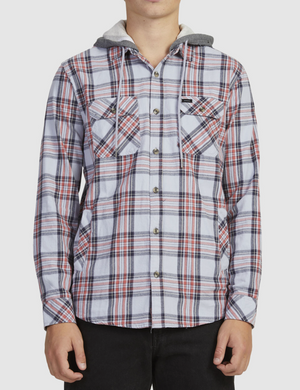 A person wears the Rip Curl Ranchero Flannel Shirt, featuring a white, gray, and red plaid pattern with two chest pockets and a hood, standing against a plain light background.
