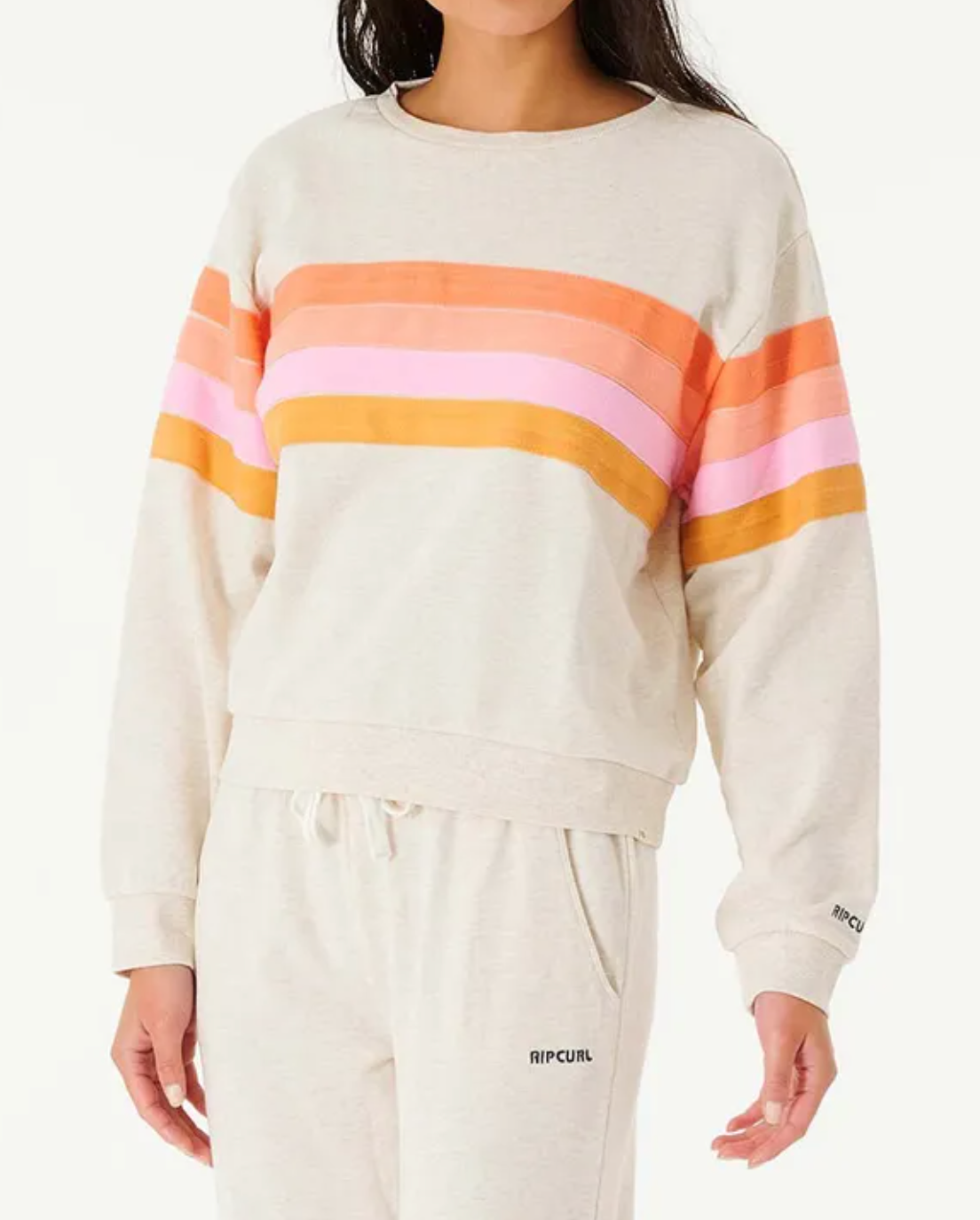 Dressed in the Rip Curl Day Break Crew, a light gray sweatshirt with orange, pink, and red stripes, a person exudes relaxed fit fashion. Paired with matching sweatpants, this outfit captures Rip Curl's signature laid-back style with its comfortable crew neck design.