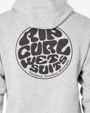 A person is shown from the back wearing a gray Rip Curl Wetsuit Icon Hood. The cozy hoodie has a prominent circular logo with the text "Rip Curl Wetsuits" in a retro, wavy font. Below the logo, three locations are listed: Torquay, Trestles, Hossegor.