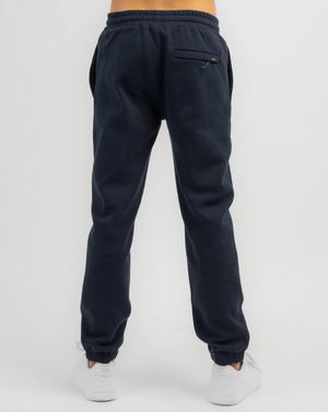 Back view of a person in Rip Curl Search Icon Track Pant, made from organic brushed cotton, with zippered back pocket, elastic waistband and cuffs. Paired with white sneakers on a plain white background, highlighting this stylish and eco-friendly choice.