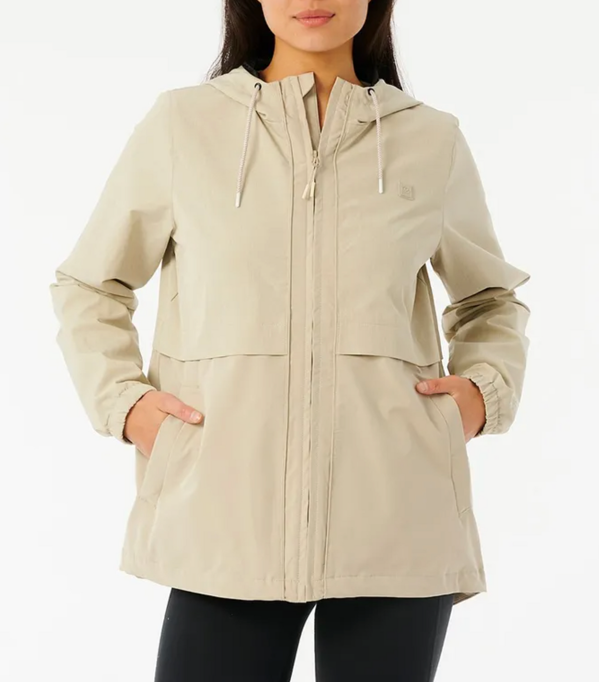 Wearing the Rip Curl Anti Series Elite III Jacket in beige, with a front zipper and two pockets, elastic cuffs, and an adjustable hood for versatility. Paired with black pants, this relaxed-fit ensemble pops against the plain white background.