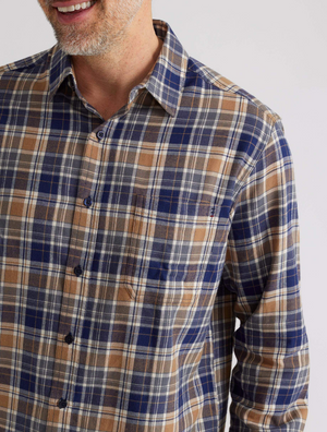 A person partially visible, smiling, wears the Breakaway Ford Cotton Brush Shirt in blue, brown, and white plaid. The 100% cotton shirt features a collar and a left-side pocket against a plain light-colored background.