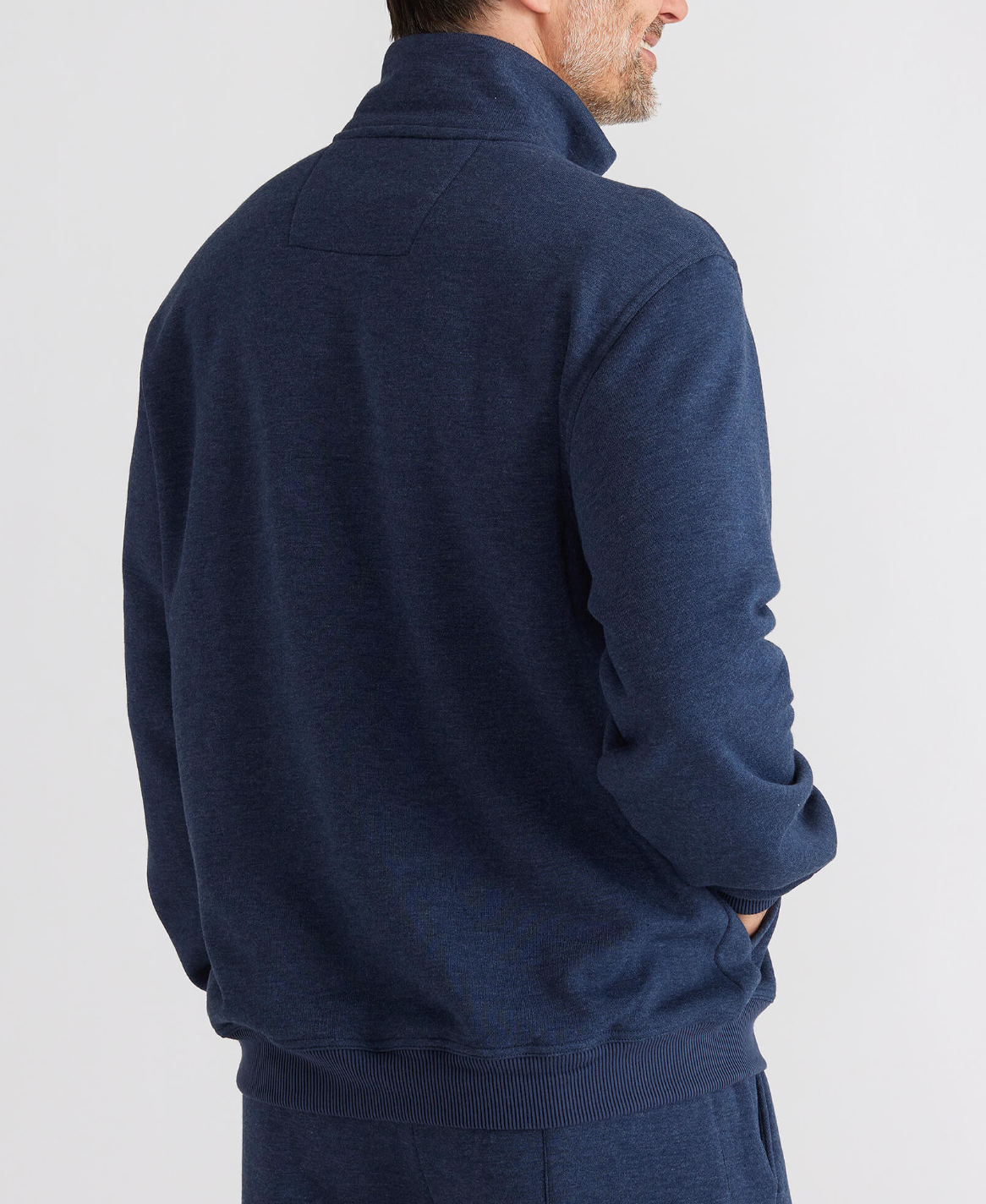 The person is seen from behind in a blue Breakaway Huxter Snowy Mt Fleece 1/2 Zip with a high collar. They have short hair and a trimmed beard, set against a plain white background.