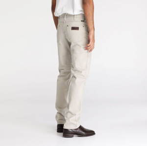 A person in a white shirt wears Wrangler Classics Straight Moleskin Jeans in light beige with visible stitching, brown shoes, and a leather patch above the back pocket featuring water-saving technology. The background is plain white.