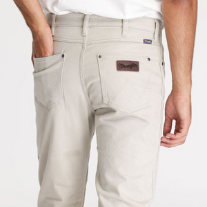 The image shows a person from behind wearing light Wrangler Classics Straight Moleskin Jeans, with their right hand in a pocket and the iconic Wrangler logo visible on one back pocket. They pair these jeans with a crisp white shirt for an effortlessly stylish look.