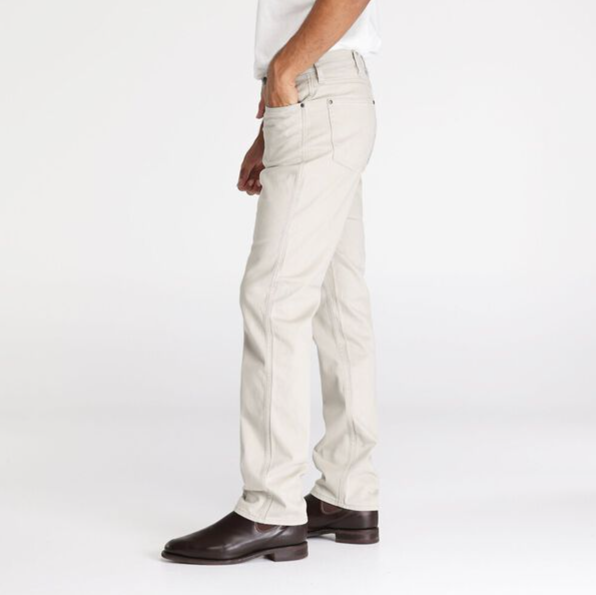 A person wearing Wrangler Classics Straight Moleskin Jeans in light beige and a crisp white shirt stands sideways with a hand in their pocket. They complete the look with dark brown leather shoes, all set against a plain white background.