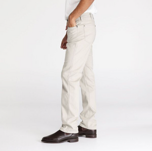 A person wearing Wrangler Classics Straight Moleskin Jeans in light beige and a crisp white shirt stands sideways with a hand in their pocket. They complete the look with dark brown leather shoes, all set against a plain white background.