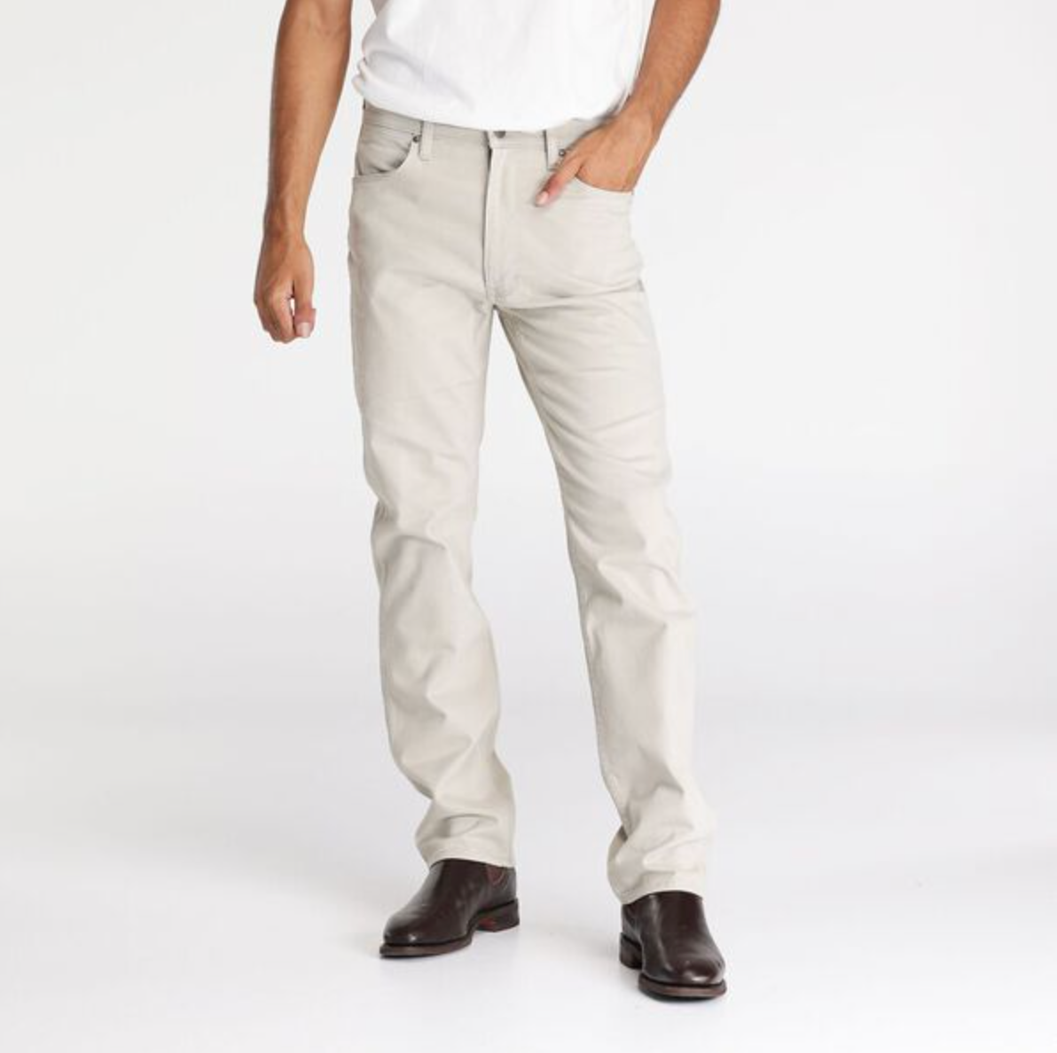 A person stands casually in Wrangler Classics Straight Moleskin Jean with a white t-shirt, one hand in a pocket. Dark brown shoes complement the outfit against a plain white background. The jeans feature innovative water-saving technology, merging style and sustainability.