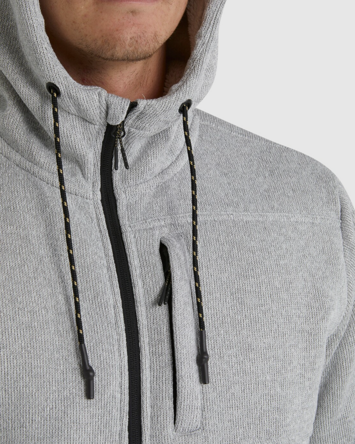 A close-up shows someone wearing the Billabong Boundary Sherpa Zip hoodie in light gray with black zipper details and drawstrings, revealing only the lower half of their face and upper torso.