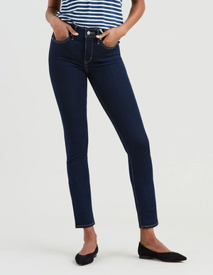Against a plain backdrop, a person models Levi's 312 Shaping Slim Jeans, featuring a tummy-slimming panel and dark blue 4-way stretch for comfort. The striped top pairs well with these stylish skinny jeans, and the look is completed with black flats and hands tucked into the pockets.