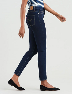A person walking in dark blue Levi's 312 Shaping Slim Jeans, recognized for their tummy-slimming panel, paired with a striped top and black flats. The image captures a side view from shoulders to feet, with slightly bent arms.