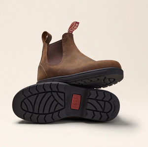 Displayed are the Rossi Endura 303 Elastic Sided Boots in brown full-grain leather with black, slip-resistant soles. One boot stands upright and the other is tilted to show its tread pattern, featuring red pull tabs with "Rossi” text for a stylish and durable look.