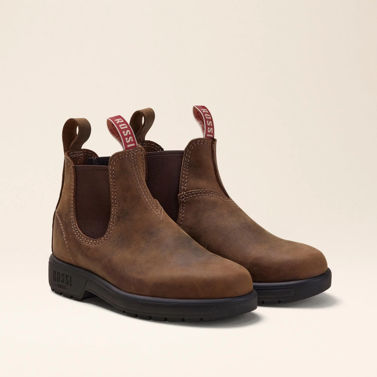 The Rossi Endura 303 Elastic Sided Boot is a brown full-grain leather Chelsea boot with "ROSSI" pull tabs, dark elastic side panels, and a slip-resistant black sole, all set against a neutral backdrop.