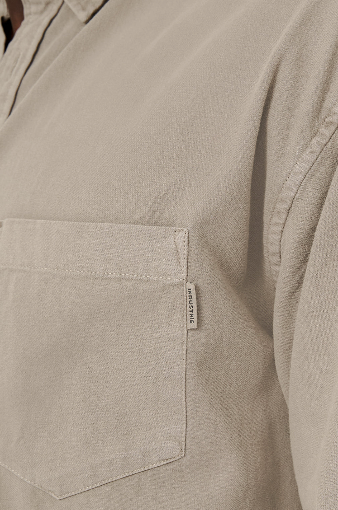 Close-up of Industrie The Taylor Shirt, a beige casual shirt with a chest pocket featuring an "INDUSTRIE" label on the side. Made from 100% cotton, it has a soft, textured fabric for comfort on any occasion.
