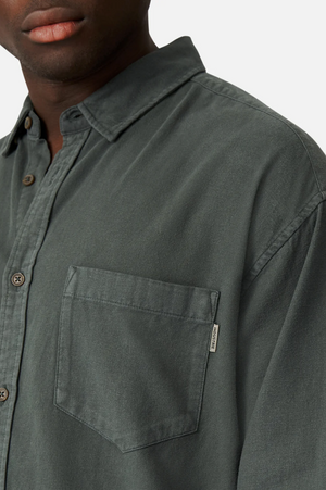 A close-up showcases a person wearing the Industrie "The Taylor Shirt" in dark green, made from 100% cotton. It features brown buttons, a chest pocket with the Industrie logo on a tag at the seam, set against a plain white background.