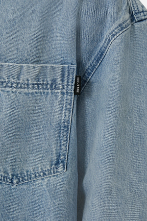 Close-up of Industrie The Lafayette Shirt in light blue denim, relaxed fit, with a visible back pocket and a small black tag stitched on the seam next to it.