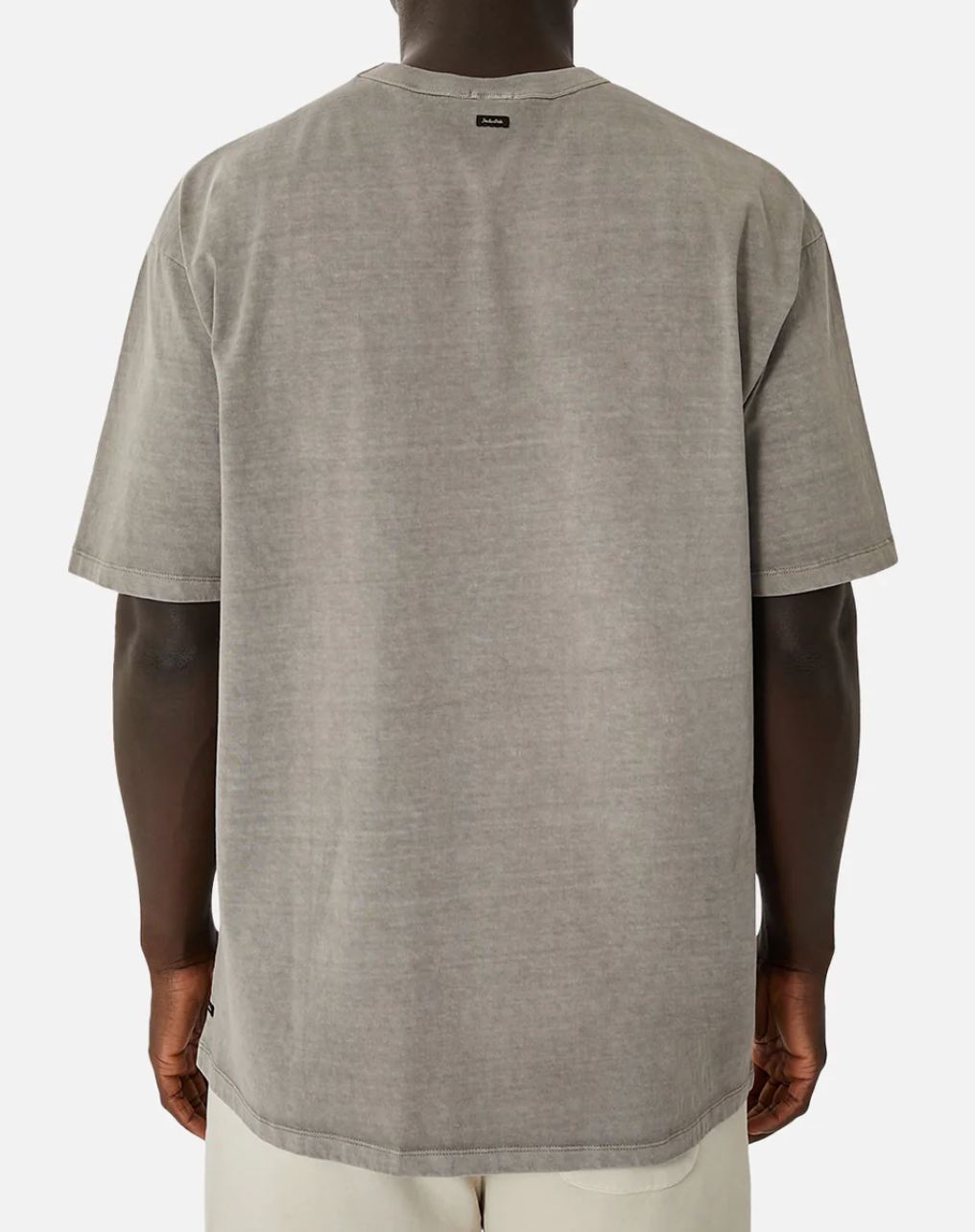 Wearing the Industrie The Del Sur Tee, an oversized, loose-fitting washed gray 100% cotton shirt with a small neck tag and seen from the back, paired effortlessly with light-colored pants against a plain white canvas for a chic look.