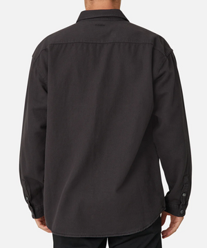 The image features the back view of a person in an Industrie The Portland Shirt, a dark gray long-sleeve button-up made from a cotton/linen blend. Its classic collar and buttoned cuffs, paired with dark pants, stand out against the plain white background.
