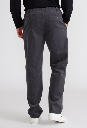 Rear view of someone sporting Breakaway Cordeaux Pant in charcoal gray with an elastic waist and two back button-detail pockets, paired with a black long-sleeved shirt and white sneakers, set against a plain white background.