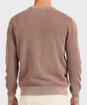 Wearing the Academy Brand Newport Crew Knit, a 100% cotton, long-sleeve beige sweater with subtle patterns and ribbed hem and cuffs, the person pairs it with light-colored pants. They're photographed from the back against a plain background.