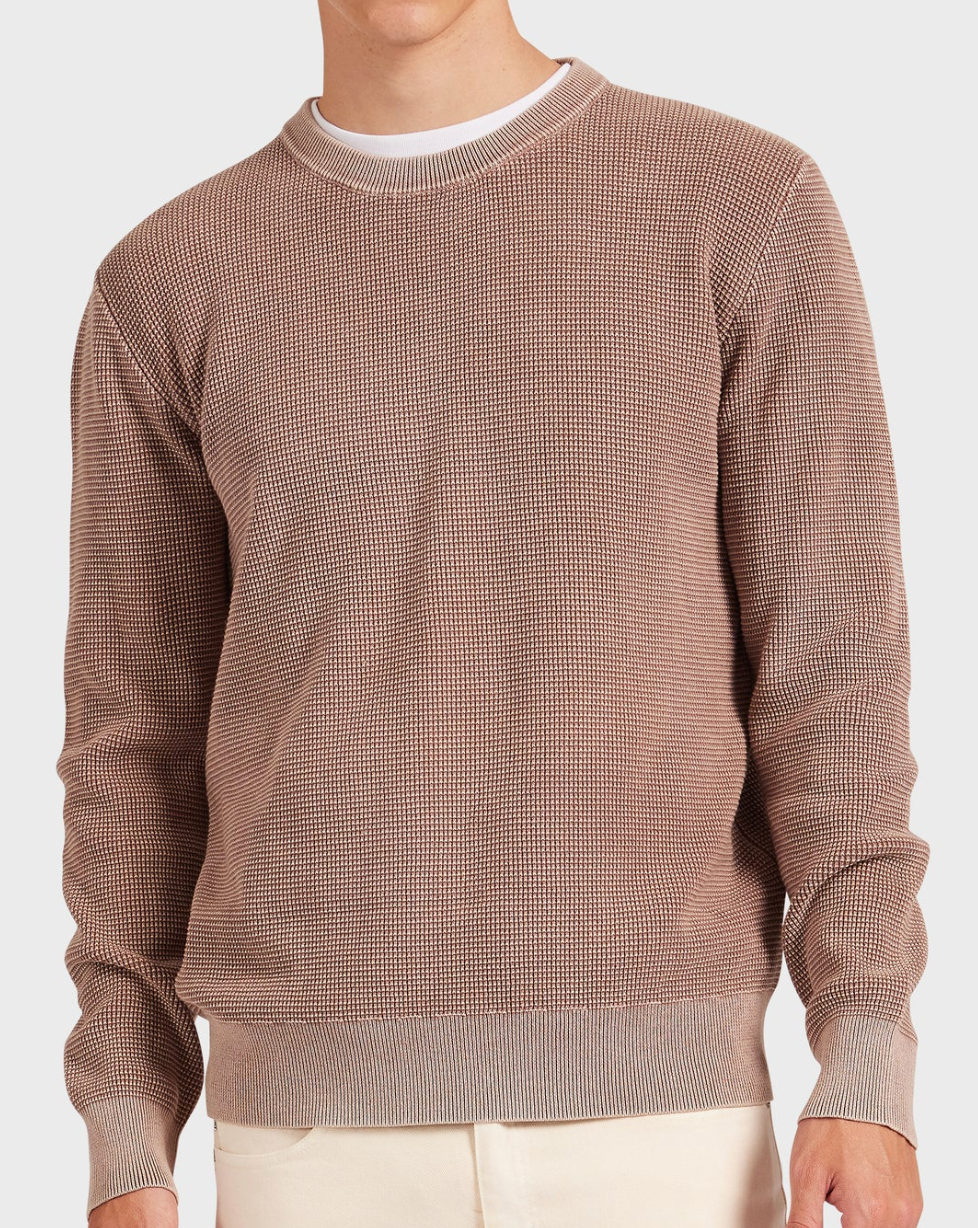 Someone wears the Academy Brand Newport Crew Knit in brown with a vintage wash over a white shirt, paired with beige pants. The view is focused on the upper body against a plain white background.