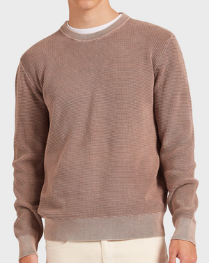 Someone wears the Academy Brand Newport Crew Knit in brown with a vintage wash over a white shirt, paired with beige pants. The view is focused on the upper body against a plain white background.