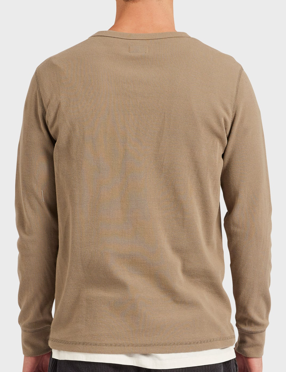 Rear view of a person in an Academy Brand Workers Crew long-sleeve, light brown shirt with rib knit texture, standing against a plain white backdrop. The outfit features dark pants and a comfy crew neck undershirt visible through their short hair.