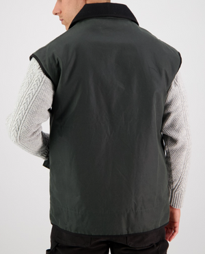 A person wearing a dark green Swanndri Foxton Vest Wool Lined over a light gray knit sweater is seen from behind. The vest, with its black collar and waterproof design, stands out against a plain white background.