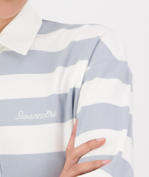 Wearing the Swanndri Carlaw Rugby shirt, a person exudes casual elegance in a crisp, white and light gray striped design with "Swanndri" embroidery. The stylish, sporty piece enhances their confident stance while only part of the torso and arms are visible.