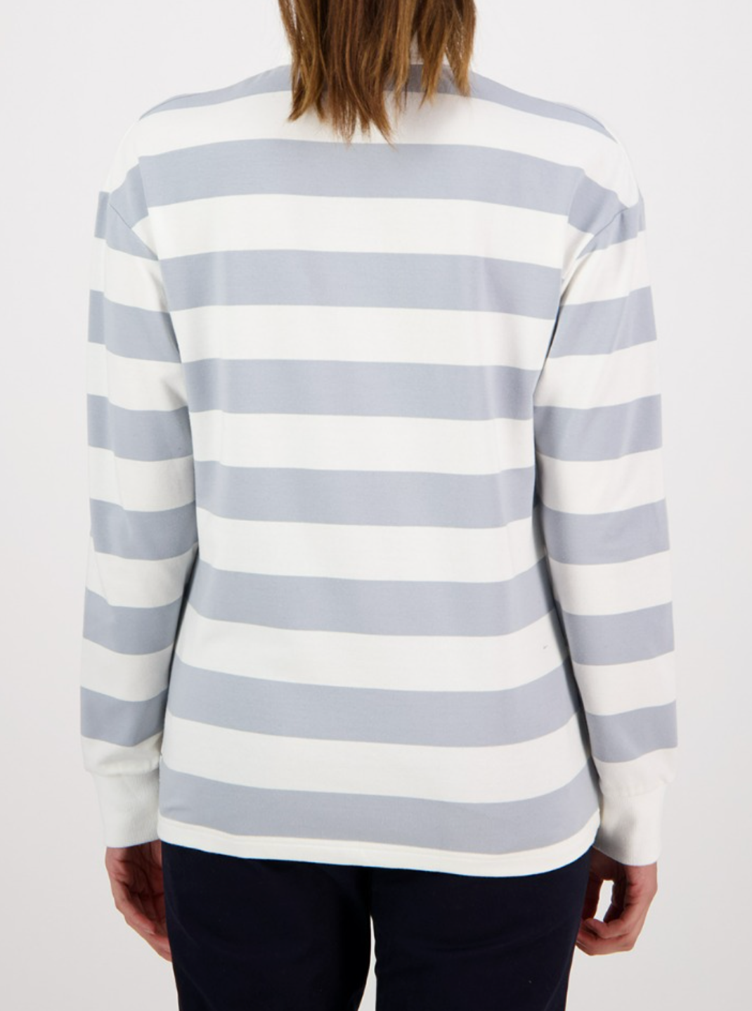 A person wearing the Swanndri Carlaw Rugby, a casual long-sleeved shirt with gray and white stripes, stands with relaxed arms and long hair. They're paired with dark pants against a plain white backdrop.